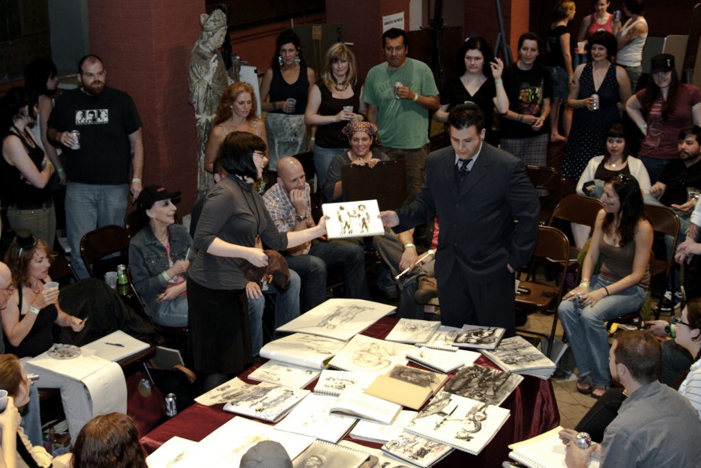 Dr. Sketchy's Philly event in 2009 at Fleisher Art Memorial. The place is packed with artists and there are sketch books on the center stage for a contest. Nicola Black is hosting with The Midwives Collective and can be seen holding up a piece as Danny Borneo chooses a winner! 